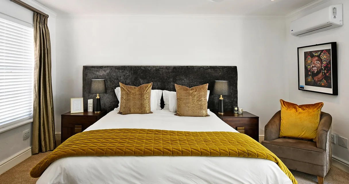 Quarto com cama arrumada, colcha amarela e poltrona ao lado, ambiente para amamentar com apoio