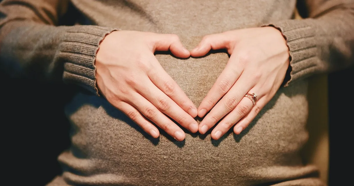 Gestante com as mãos em formato de coração sobre a barriga